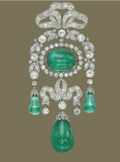 BELLE EPOQUE EMERALD AND DIAMOND BROOCH, BY CARTIER Of garland design, centering upon a cabochon emerald in a circular-cut diamond surround, suspending a diamond-set ribbon with drop-shaped emerald pe…
