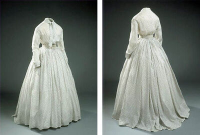 Day dress, ca. 1860s, in a white jaconet print with narrow lace trim. Two glass buttons in the front; loose belt with rosette, edged with lace. National Museum of Denmark