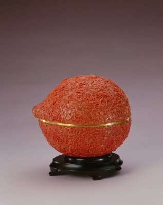 金胎珊瑚桃式盒，清，高19cm，长22.5cm，宽20cm。 盒为桃形，分为器和盖两部分。盒内为金胎，外为红珊瑚面，满琢纹饰。顶中部琢一篆书团“寿”字，字上面凸雕一展翅的蝙蝠，寓福寿之意。盒上半部琢云气纹，云气中有9…