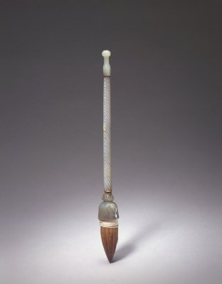 青玉绳纹管提笔，通长28.3cm，斗径2.9cm。 笔头为褐色笋尖式。笔管青玉质，浮雕旋转状绳纹。笔斗壁上阴刻四枚荷瓣，宛如荷花盛开，管顶圆雕的荷苞与之呼应。 笔头与笔管通过金属连接，笔斗的颈部镶嵌数颗红色宝石及金属装饰。此种工艺富有浓郁的痕都斯坦风格。笔管的玉色较笔斗略显浅淡，但工艺风格与笔斗浑然一体…