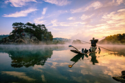 雁荡山世界地质公园的清晨，水面上萦绕着丝丝缕缕的薄雾，晨曦映红了朝霞，也点亮了水面。赶早的渔翁，悠悠的撑着竹排，载着的鸬鹚，在楠溪作业，憨厚的汉子在镜头前面，还是下意识的别过了头。