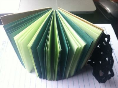 露出书脊的手工本子，内页采用深浅两种绿色交替。钩花片配上木扣子，可以将本子扣住。
