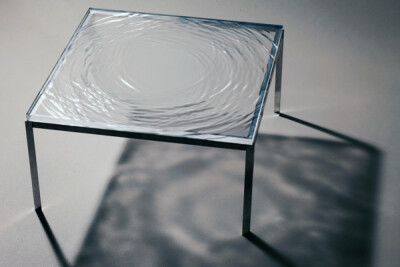 工作在德国柏林的瑞典建筑师兼艺术家 Fredrik Skåtar 设计了一组水波桌子，桌面用透明的有机玻璃雕刻而成，看上去仿佛是一滴水滴入水面，泛起层层波纹。