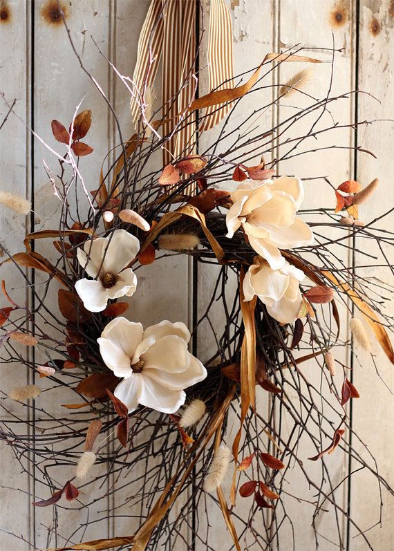 Lifelike ivory magnolia flowers are featured and complemented by fuzzy dried hare's tails. Rust-hued dried grasses reflect the subtly metallic copper leaves. Suspended by an elegant caramel and ivory striped grosgrain ribbon and topped with a bow,