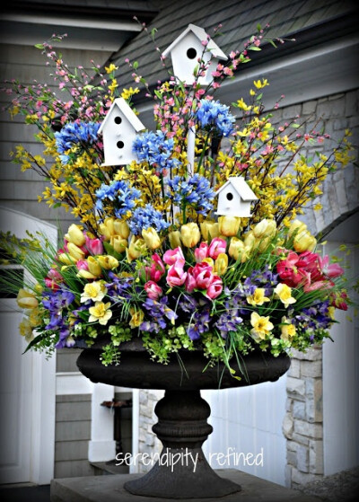 Spring urn planter flower arrangement with forsythia tulips daffodils and white bird houses.