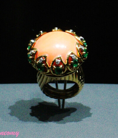 【戒指】(1947年，卡地亚巴黎)工艺：用黄金和铂金制作，戒面为一颗凸圆形珊瑚，周围镶嵌一圈方形刻面祖母绿和明亮式切割的钻石.历史：为英国温莎公爵夫人特别订制