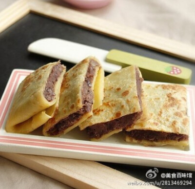 【红豆煎饼】1.和面糊用的原料，将原料调匀成面糊；2.案板上铺上保鲜膜，将红豆沙在保鲜膜上压平并弄成正方形；3.加热油锅，将面糊倒入形成圆形，用小火慢煎，两面煎熟；4.将方形的红豆沙放在圆煎饼中央；5.将饼皮的…