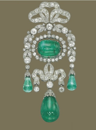 BELLE EPOQUE EMERALD AND DIAMOND BROOCH, BY CARTIER Of garland design, centering upon a cabochon emerald in a circular-cut diamond surround, suspending a diamond-set ribbon with drop-shaped emerald pe…