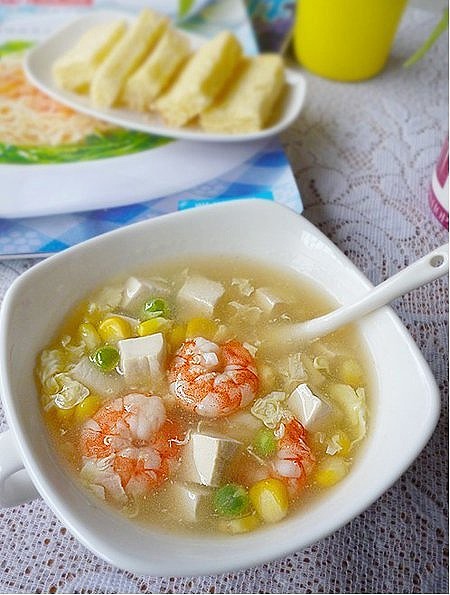 三鲜豆腐羹 材料 嫩豆腐 豌豆粒 鸡蛋 胡椒粉 生粉 鲜虾 玉米粒 盐 鸡粉 作法1.豌豆和玉米粒洗净焯一下水2.豆腐切小块3.鲜虾剥壳去黑线4.鸡蛋打好备用5.锅里放适量水6.水滚后放入豆腐略煮一会7.随后放入豌豆和玉米粒，煮至断生8.放入虾仁略煮一会9.放入一点盐和胡椒粉调味10.之后用生粉勾一个薄欠11.煮到有些浓稠后，沿着锅边倒入打好的鸡蛋12.先不要翻动，等鸡蛋稍微凝固了再稍微翻动下就可以了