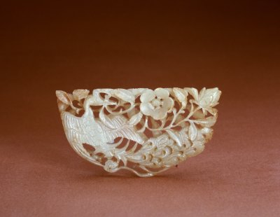 玉孔雀衔花饰，宋，长7.6cm，宽3.8cm。清宫旧藏。 花饰玉色青白，有赭色斑，为半圆形玉片，其上透雕孔雀衔花图案。图案主体为孔雀，孔雀回首，拖尾，展翅，口衔花枝，枝上有花两朵，品种不同。 花鸟类玉器在宋、辽、金的考古发掘中多有出土，其中不乏鸟翅一只伸开、另一只下折的造型，这种鸟衔花玉饰是宋代较流行的样式。北京房山石棺墓出土有孔雀形玉发饰，孔雀之尾端带有半月状透空孔洞，同此件作品孔雀尾部的表现相同。此件作品较一般宋代花鸟玉佩更为精致，据其形状，可能是一种嵌饰。