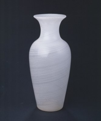 缠丝玻璃瓶，高30.4cm，口径10.5cm，底径8.5cm。 瓶圆形，长身，喇叭口，细颈，丰肩，平底。通体以无色透明玻璃和白色不透明玻璃相间，作均匀的条带状，呈螺旋上升之势。 此瓶为吹制，壁薄体轻，材精形美。瓶身以白色与无色透明玻璃作装饰，清爽素雅。其纹理旋转流动，极富韵律美。这种装饰新奇独特，极为罕见。