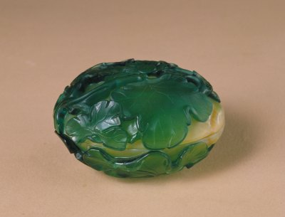 黄地套绿色玻璃瓜形盒，高4.7cm，口径7.7×8.3cm。清宫旧藏。 此盒为扁圆形，以黄色玻璃作胎，黄色之中有红色与黄色相搅而成的丝状，外套透明绿色玻璃为花纹。盒外表覆盖有绿色玻璃瓜叶纹，藤蔓突出，叶脉清晰，花瓣舒展，一只小虫栖息于叶上。 此盒的形状如一绿叶下覆盖的甜瓜，匠艺独到。玻璃质地晶莹透亮，光泽度好，有宝石的效果。