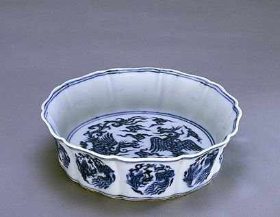 青花鸾凤纹葵瓣式洗，高4.5cm，口径17.5cm，足径14.2cm。 洗呈五葵瓣形，里心微凸起。通体青花装饰?？谘啬谕馐吻嗷ㄋ呶?，里心绘凤、凰各一只，间以朵云。外壁绘团形凤凰10组，与葵瓣式器身相对应。底青花双圈内有“大明宣德年制”六字双行楷书款。 此器造型别致，釉质莹润，青花色调浓艳，工艺技法娴熟