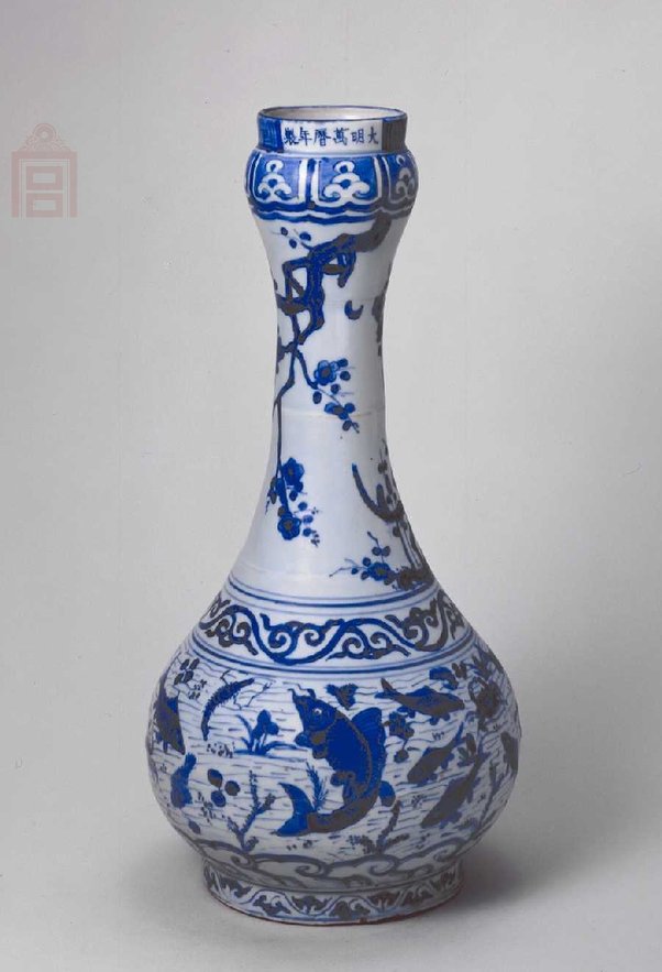 明万历 青花鱼藻纹蒜头瓶，明万历，高37.5cm，口径7.7cm，足径18cm。 瓶直口蒜头式，长颈，溜肩，圆腹，圈足。直口下蒜头部分饰莲瓣纹，颈部饰花卉纹，肩部饰一周卷枝纹，腹部绘鱼藻纹。鱼儿呈各种姿态游弋，衬以淡色细笔绘出的水波纹，生动自然。口部书写“大明万历年制”六字横款。