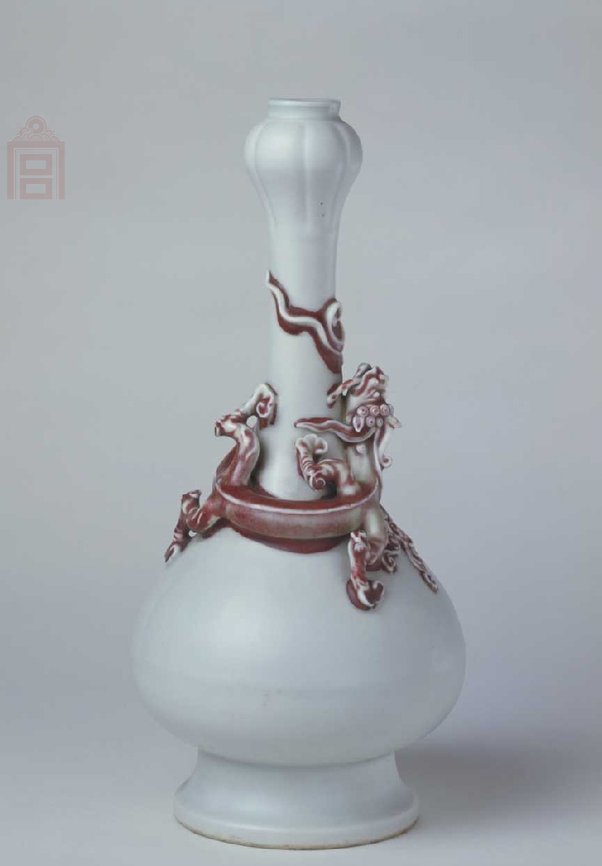 明嘉靖  白釉塑贴红蟠螭纹蒜头瓶，明嘉靖，景德镇窑制品，高30cm，口径2.6cm，足径10cm。清宫旧藏。 瓶口呈蒜头形，细长颈，溜肩，鼓腹，高圈足外撇。瓶通体施白釉，釉质洁白细润。口部刻细线蒜瓣纹，腹部有粘接痕一周。瓶颈至肩部塑贴一条红色螭龙，曲体上仰，口衔仙草，由肩部向颈部盘绕，卷尾与首相接，四肢平伏于瓶肩部。