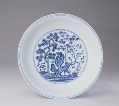 明宣德 青花松竹梅纹盘           青花松竹梅纹盘，明宣德，高4.2cm，口径21.4cm，足径13.6cm。 盘撇口，弧壁，圈足。内外皆有青花纹饰。盘心环以青花双圈，内绘松、竹、梅、山石、灵芝等纹饰。外壁绘庭园景色，远方仙山云气缥缈，近有悠闲的贵妇等人物凭栏而立，以山水、杨柳等景物相衬。口沿和足边各饰青花弦纹两道。圈足内施白釉，中间青花双圈内书“大明宣德年制”双行六字楷书款。