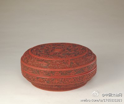 剔彩云鹤寿字纹圆盒】明嘉靖，高14.2cm，口径32cm。盒圆形，平盖面。剔彩备红、绿、黄等色。盒内、外底均髹黑光漆，外底正中刻填金楷书“大明嘉靖年制”六字款。此器纹饰雕工快利，漆色深沉，款识内戗金，这些均为嘉靖雕漆的典型特征。