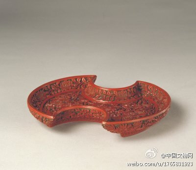 绿地剔红双龙纹圣寿万年盘】东明嘉靖，高4.2cm，最宽径25.9cm。盘为银锭式，红漆雕双龙捧宝盆图案。盘中心有“圣寿万年”四字，足内刻楷书“大明嘉靖年制”横行款。此盘造型为嘉靖时期出现的新形制，是一件代表嘉靖…