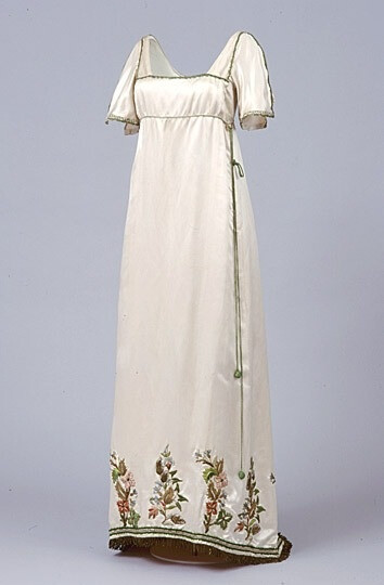 Neo-Regency. Embroidered cream satin fancy dress imitating regency gowns evening gown, British, 1913. It is made of cream satin, with a low décolletage edged in green and gilt braid. The hem is trimmed with gilt fringed braid and hand appliquéd Turkish style embroidered motifs.