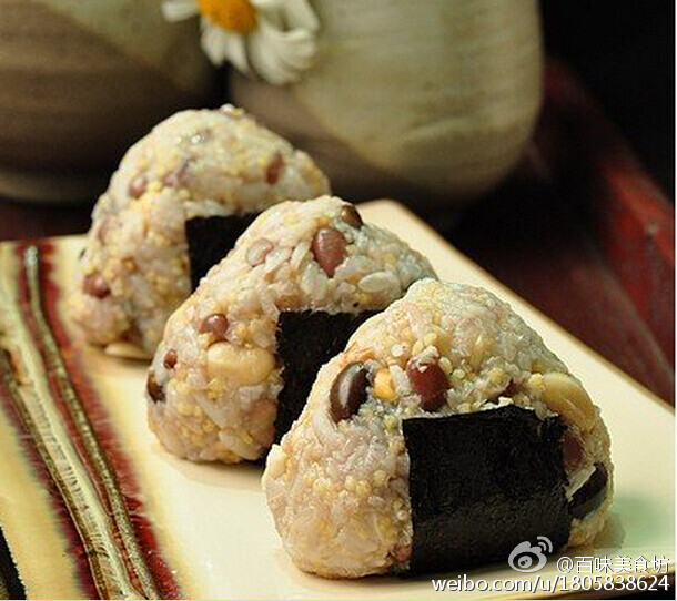  【五谷饭团】黑豆，红豆，黄豆，隔夜泡发。泡好的三种豆，再加入适量的洗净的糯米和小米。放入电饭锅内煮成米饭，煮好的杂粮饭，放凉。花生炒熟敲成花生碎。白芝麻炒熟。加入适量的盐和花生碎拌成馅料。取一小块米饭，放在保鲜膜上，按扁，包花生芝麻馅。封好口，然后捏成三角形。底部包上一小块海苔。 @百味美食坊