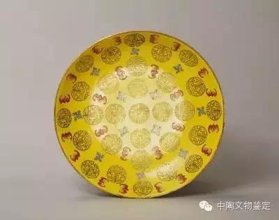 黄地红蝠金彩团寿字纹盘，高5.7cm，口径27.9cm，足径17.1cm 珐琅彩：是康雍乾极为名贵的御器，俗称“古月轩”瓷器。明永乐时期开始有种工艺在铜胎上以蓝为地色，掐以铜丝，填上红黄蓝绿白色釉烧成，其蓝色以景泰年间最好，故称景泰蓝。进口珐琅彩效果与景泰蓝相似。流行铜胎、玻璃胎、瓷胎、紫砂胎画珐琅，珐琅彩瓷器创烧于康熙，大都是一些日用小器。