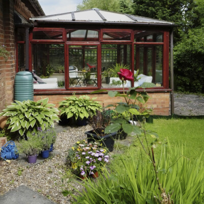 Here is an attached greenhouse with a foundation and glass for its glazing. This greenhouse is large enough to have some seating. It's a perfect year round escape into a lovely verdant garden.