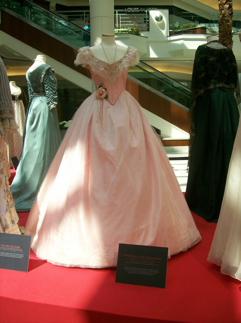 电影《歌剧魅影》中化装舞会一幕女主穿的舞裙。1860年代后期晚装款式，非常长的裙摆。柔美的粉色绸裙，外罩一层点缀水钻的薄纱。后摆上有两处收束，装饰着美丽的粉红色大花和丝带。上衣领子上有一圈精致的蕾丝和小花蕾。这件衣服的色彩运用得格外好，甜甜的但又很清爽，十分悦目。这是设计了《劝导》、《伊丽莎白》两部曲和《爱玛》等古装佳作的亚历山德拉·拜恩的作品。