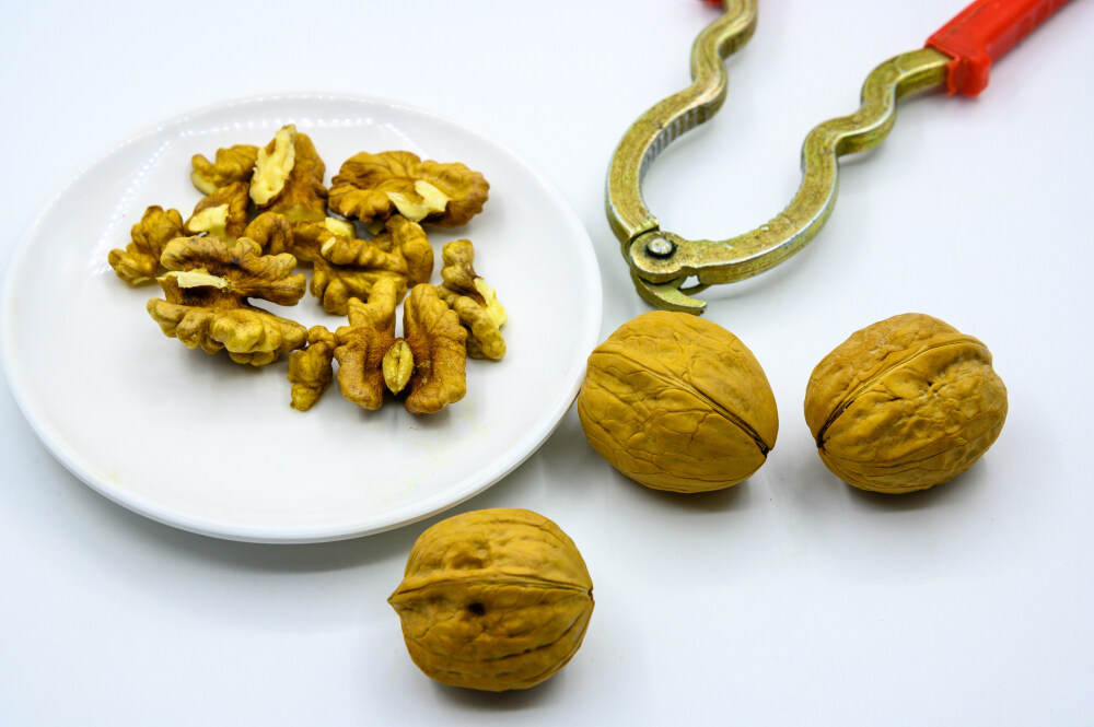 食品 食物 植物 果实 成熟的 特写 绿色食品 美味 零食 坚果 干果 核桃 核桃仁 膳食纤维 小吃 益智 亚洲 健康食物 有机食品 膳食 养生 滋补 营养 食材 生活方式 健康的 白色背景 白瓷盘 干果钳 简单背景
