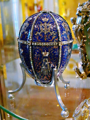 沙皇十二纹章彩蛋 Twelve Monogram Egg 制作于1896年，这是 沙皇尼古拉二世 送给 母亲皇后玛利亚 Nicholas II to Empress Maria Feodorovna 的一枚彩蛋，用半透明蓝色珐琅制作，钻石将蛋壳分割成玫瑰式花瓣，共有12块区域，上半部的六面用钻石镶嵌出沙皇亚历山大三世的皇室纹章图案。蛋壳的下半部的上方则是钻石镶嵌而成的皇后玛丽亚芙娜的皇室纹章。
