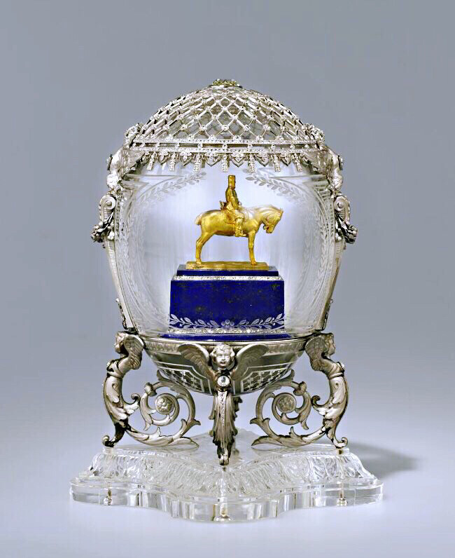 法贝热 Fabergé 制作的 亚历山大三世骑士复活节彩蛋 ‘Alexander III Monument’ Easter Egg 1910年复活节 尼古拉二世皇帝送给玛丽亚·费奥多罗夫娜皇后 用黄金、白金、钻石制作，彩蛋内的微型人物肖像是由青金石雕刻。这是彼得堡亚历山大三世纪念碑的一个微缩复制品，骑士建立在一个矩形基座上，青金石镶了两行的玫瑰。该彩蛋的顶部有一颗超大钻石，并刻有制作年份1910。托架由青金石雕刻的小天使和扭曲的花枝组成，整个彩蛋和托架安放在玫瑰花瓣形状的水晶基座上。