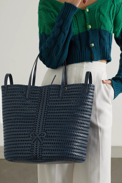Anya Hindmarch 这款 “Neeson” 手提包以纤细的皮革条手工制成，整个制作工序需耗费超过十二小时。正面的蝴蝶结编织图案颇具品牌特色，无衬里设计令包身更加轻盈，内置贴袋还可稳妥保管你的钥匙、唇膏和银行卡。