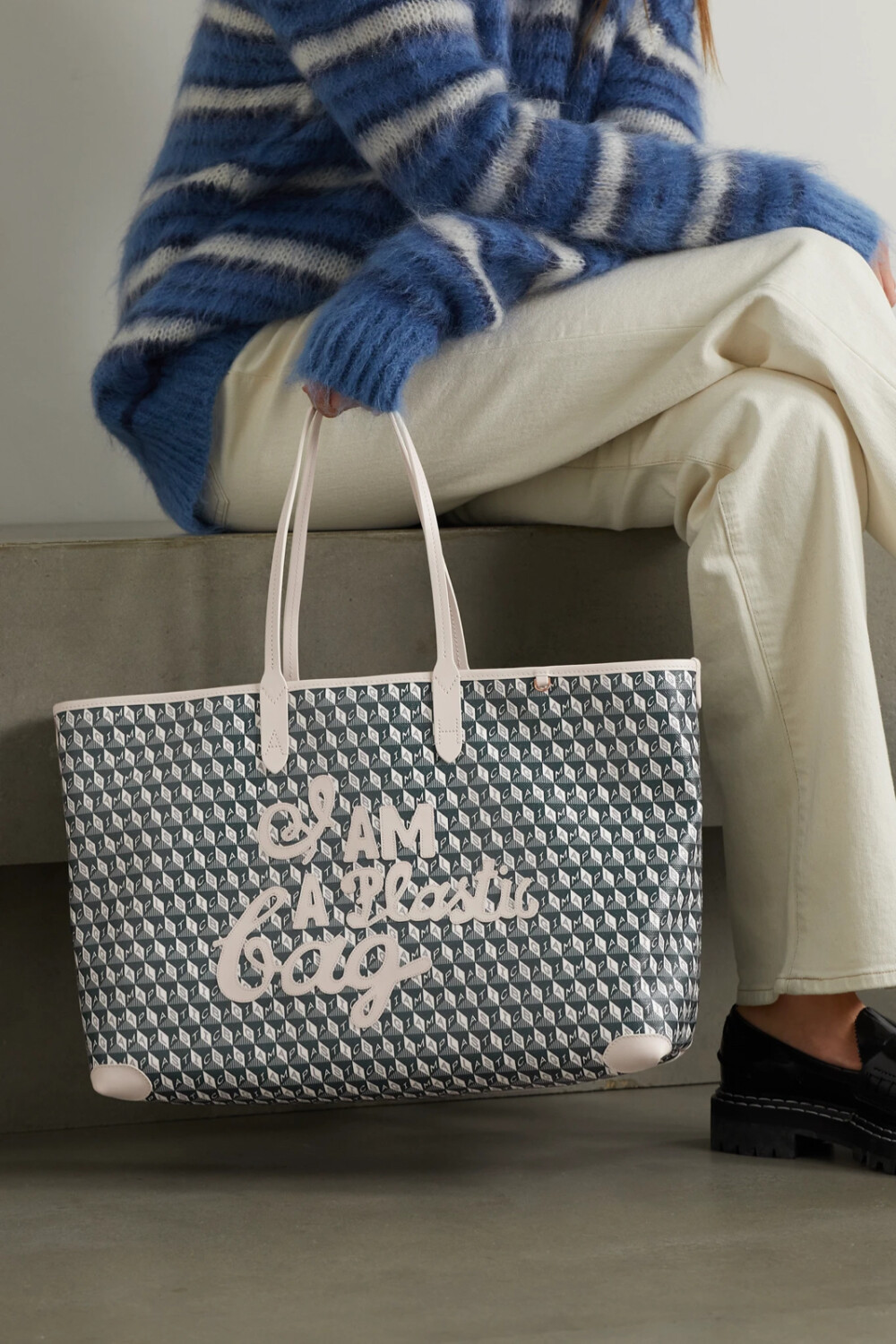 这款手提包出自 Anya Hindmarch 著名的 “I Am A Plastic Bag” 系列，采用 32 个废弃塑料瓶打造而成。这些回收再生的纤维被织入耐磨帆布之中，再经过涂层处理，可从容应对各种天气的考验。包身印有品牌首字母 “AH”，并以白色皮革饰边，包内还设有拉链口袋。