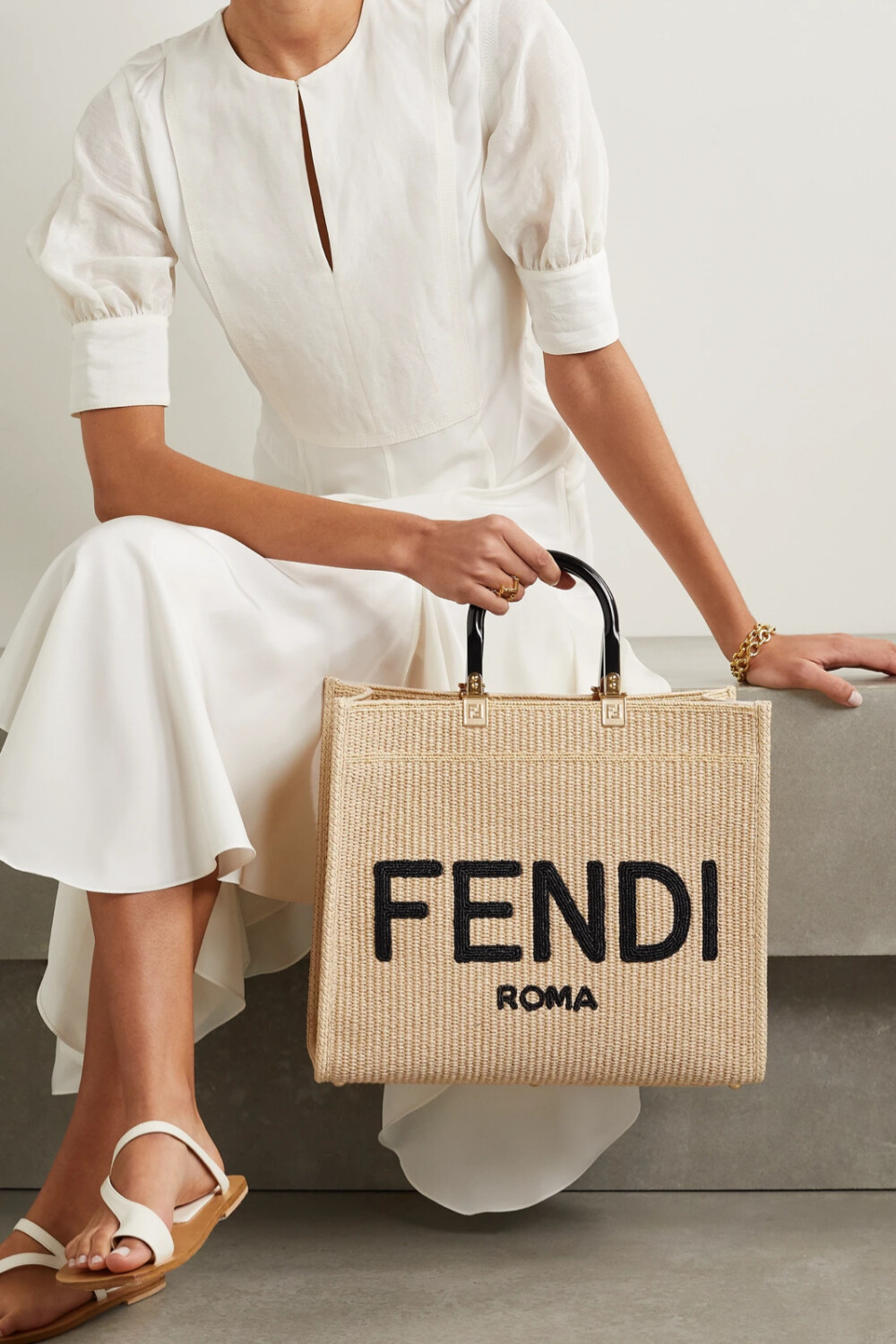 Fendi 这款 “Sunshine Shopper” 拉菲草手提包诞生于品牌的意大利工坊，织有醒目的黑色 Logo，亚克力手柄上还低调缀有经典的金色 “FF” 标志。包内容量充裕，足以妥善收纳笔记本电脑、备用高跟鞋等日常必备物品。