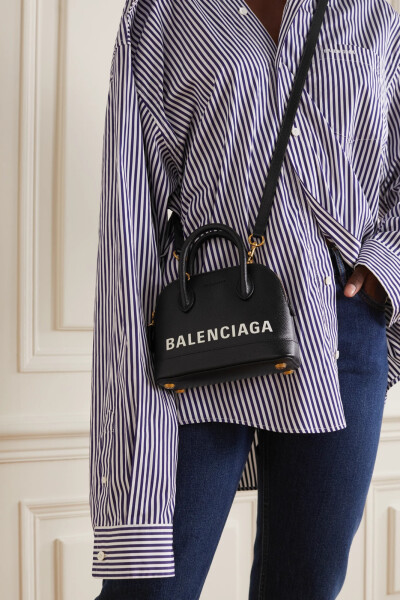 Balenciaga 以复古包袋为原型打造出这款 “Ville” 手提包，弧形包柄与半圆形包身相辅相成，倍显立挺。它采用纹理皮革制作于意大利，印有白色品牌字母 Logo，肩带可自由拆卸。