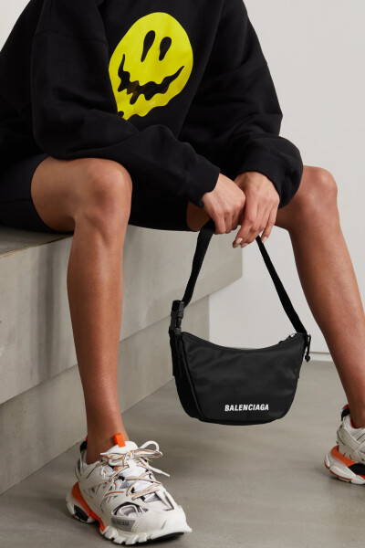 Balenciaga 这款 “Wheel Sling” 单肩包采用耐磨的黑色软壳面料在意大利制成，其上绣着品牌名称。单品柔软松垮，包内空间紧凑合理，拉链隔层方便归置随身物品。不妨随心调整肩带长度。