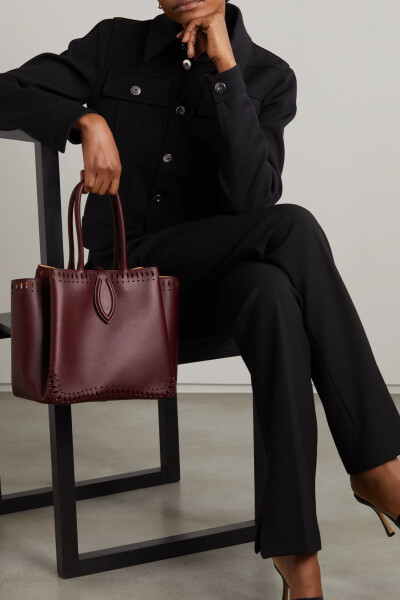 Alaïa 这款 “Angèle 25” 手提包包侧的折叠细节立体别致，品牌更是以优雅连衣裙的波浪垂褶比喻其美态。单品以柔滑皮革制于意大利，花瓣状激光雕花勾勒出包型。绒面革内里随附可拆卸小袋，能用于存放零钱和钞票。它…