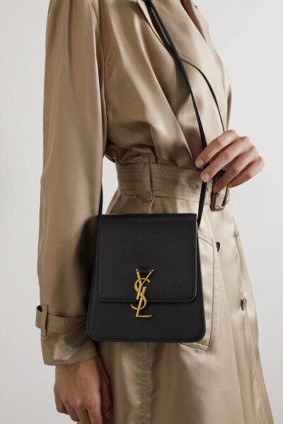 SAINT LAURENT 将 “Kaia” 马鞍包与 “North South” 手提包巧妙相融，打造出了这款优雅大方的单肩包。单品以柔滑的黑色皮革于意大利制成，梯形包身立体有型，正面翻盖上点缀有时装屋经典的金色标志搭扣，内置滑袋…