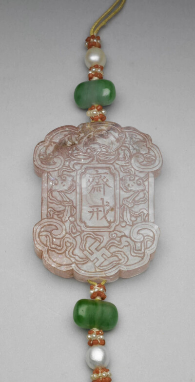 清 粉红碧玺斋戒牌，牌长5.15公分，长31公分，宽4.05公分，厚0.8公分，台北故宫博物院藏。
两面中央各刻“斋戒”及满文斋戒同义字，周琢螭蝠、卍、灵芝、桃纹等，上下繫黄线，贯饰珍珠、翠玉、红白米珠等，下端饰结…