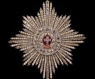 丹麦王室红十字之星徽章由白金长条镶嵌珍珠和钻石打造而成，模拟光芒万丈的视觉效果，象征一国的荣耀