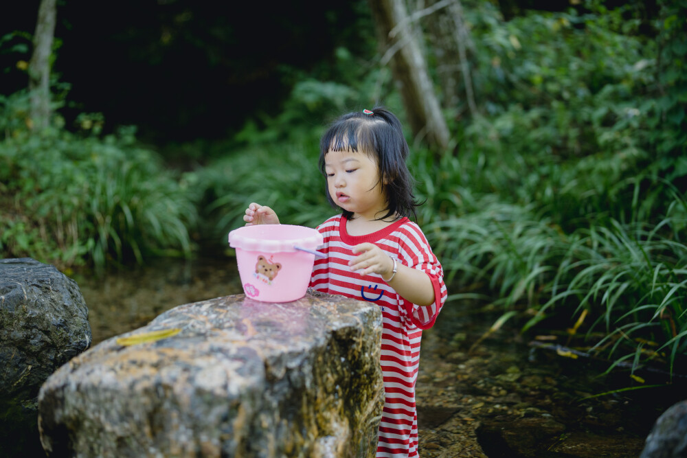 避暑还是要选九溪呀
摄影：洪小漩
出镜：菲比和爸爸
好多年前，九溪还是一个小众的徒步纳凉处。以前一道来的都是美少女，拍些清凉的照片。
而今，九溪火得很突然，纵使我们起了个大早，七点多就抵达，却已经有不少以家庭为单位出游的人，早一步抵达，人均一直水枪，玩得不亦乐乎。
对于菲比而言，这是她第一次体验九溪的快乐。仅一只粉色小桶，就让她乐不可支。22个月的她会说“还要玩”“没有鱼”“冰冰凉”“呦呦切克闹”，以及会将打满水的水桶递给新认识的小男孩说“哥哥帮我拿拿”，小奶音，超好玩。
作为初体验，她负责快乐，我和阿科负责后勤保障。但是我们工作不到位，带足了裤子，没带够衣服。面对在水里玩得湿透的