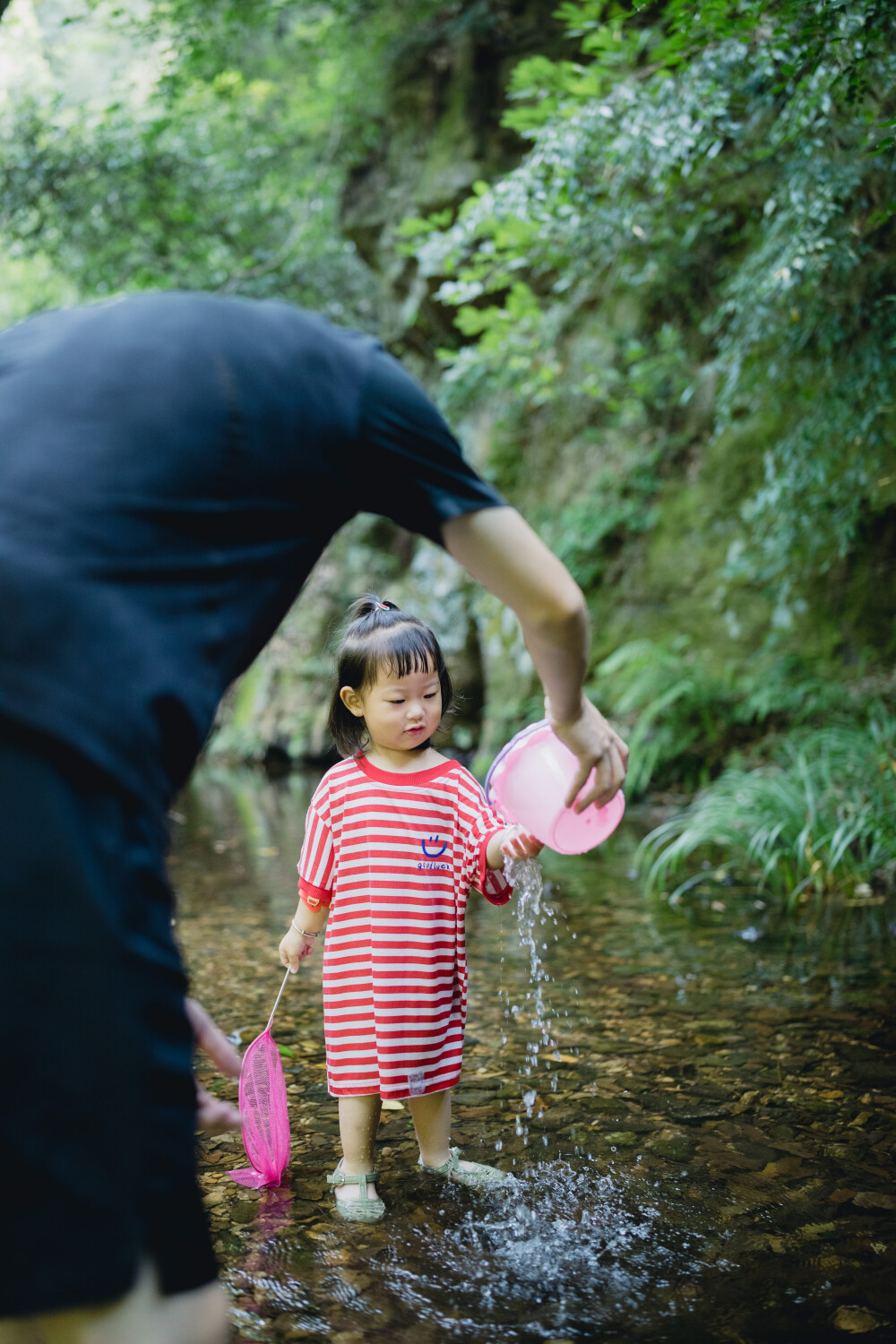避暑还是要选九溪呀
摄影：洪小漩
出镜：菲比和爸爸
好多年前，九溪还是一个小众的徒步纳凉处。以前一道来的都是美少女，拍些清凉的照片。
而今，九溪火得很突然，纵使我们起了个大早，七点多就抵达，却已经有不少以家庭为单位出游的人，早一步抵达，人均一直水枪，玩得不亦乐乎。
对于菲比而言，这是她第一次体验九溪的快乐。仅一只粉色小桶，就让她乐不可支。22个月的她会说“还要玩”“没有鱼”“冰冰凉”“呦呦切克闹”，以及会将打满水的水桶递给新认识的小男孩说“哥哥帮我拿拿”，小奶音，超好玩。
作为初体验，她负责快乐，我和阿科负责后勤保障。但是我们工作不到位，带足了裤子，没带够衣服。面对在水里玩得湿透的
