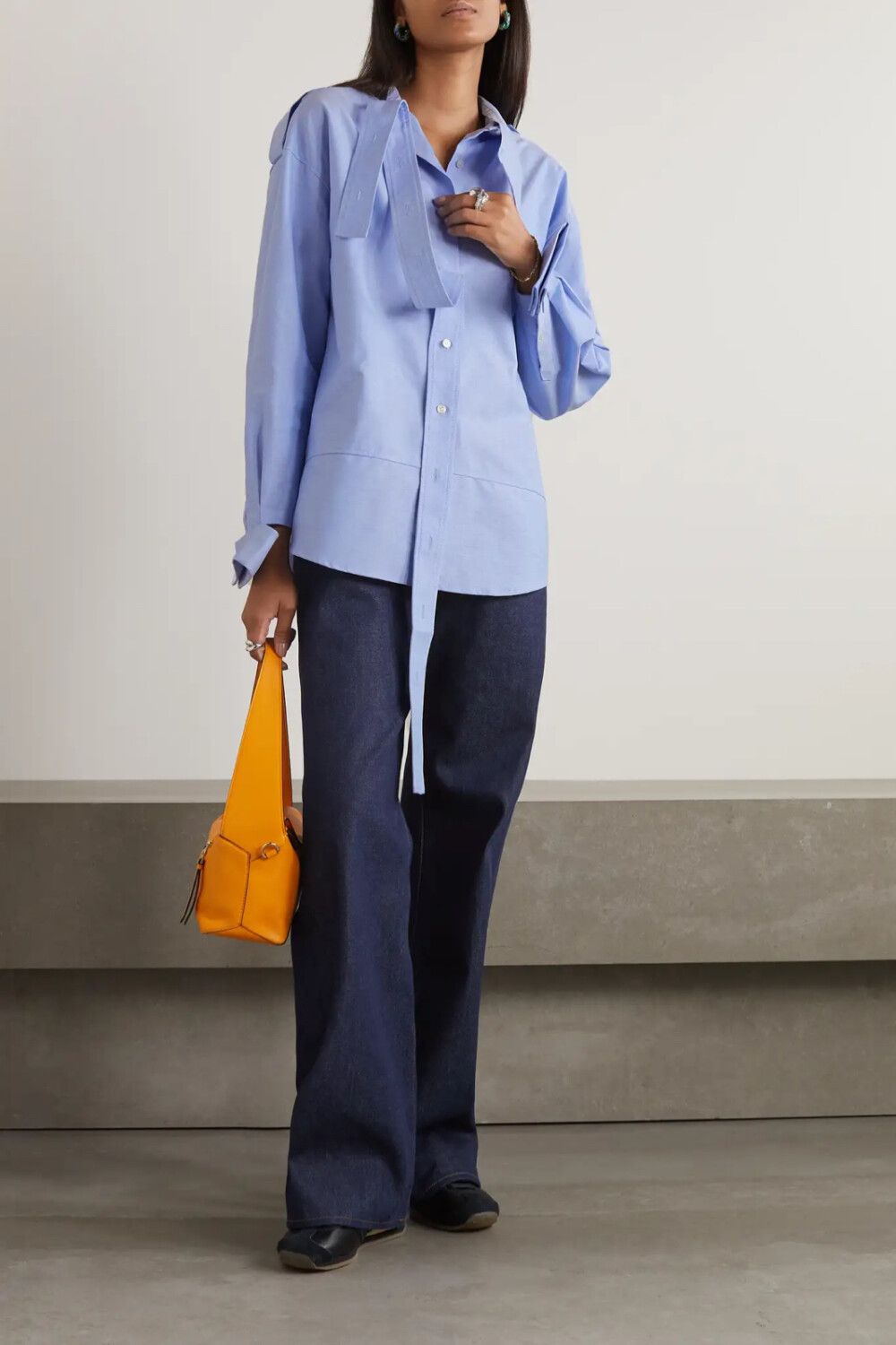 Meryll Rogge 这款衬衫以浅蓝色纯棉钱布雷布制成，从衣领垂落至门襟中央的长带和“脱落”的立挺袖口释放出前卫的解构酷感。不妨束入牛仔裤或阔腿裤穿着。