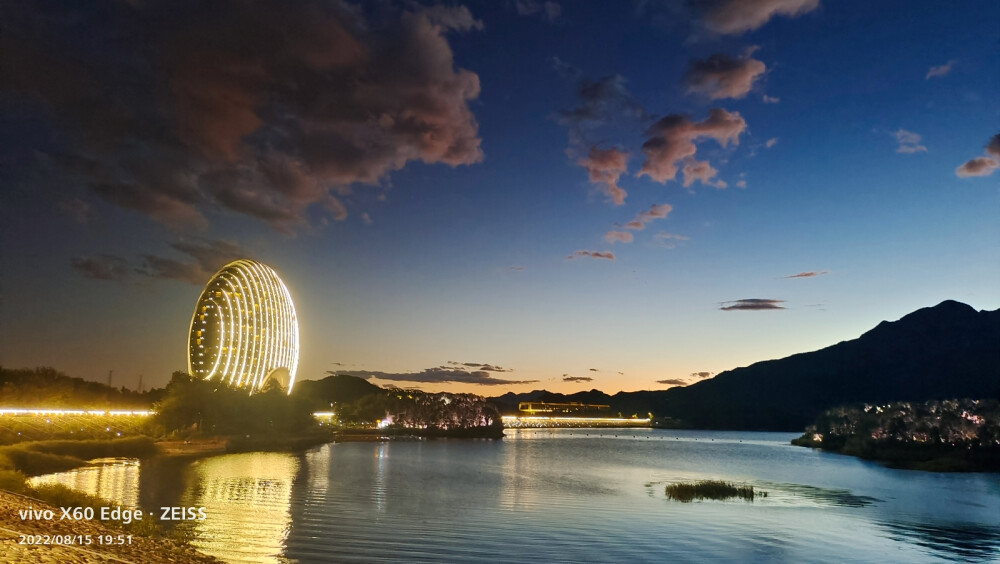 在北京怀柔区的雁栖湖边，吹着夜风，赏着夜景，波光粼粼，落日余晖就像颜色滤镜一般过渡柔和，云朵非常配合，飘在了合适的位置。