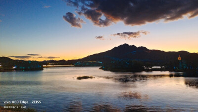 在北京怀柔区的雁栖湖边，吹着夜风，赏着夜景，波光粼粼，落日余晖就像颜色滤镜一般过渡柔和，云朵非常配合，飘在了合适的位置。