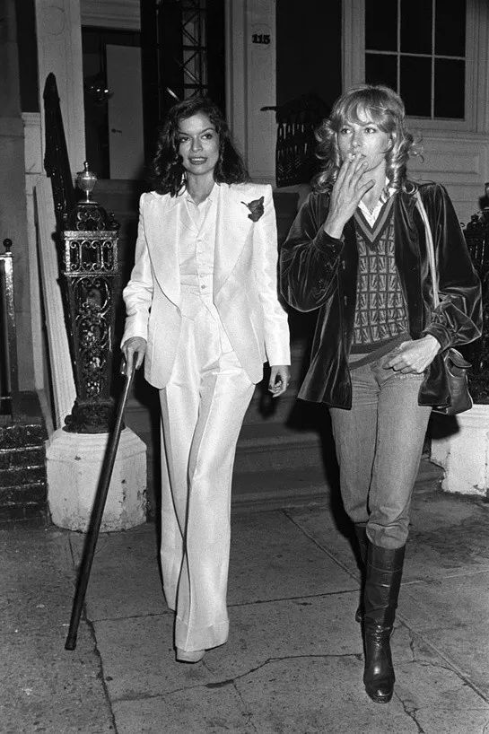 ▲ 1974年纽约，比安卡·贾格儿 (Bianca Jagger) 穿着候司顿 (Halston) 白西装和著名影星Nathalie Delon一起外出。Delon的穿搭也超好看。