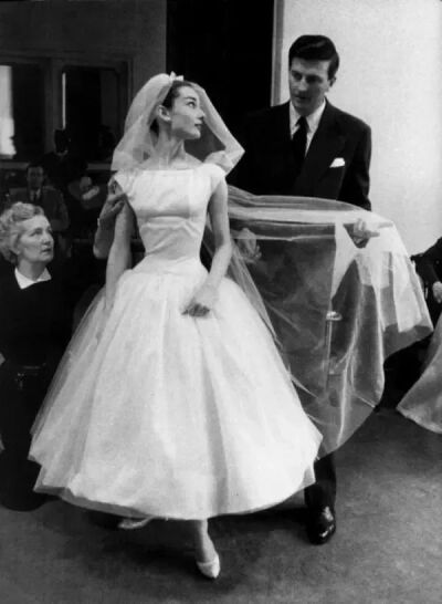 ，纪梵希先生不愧是知交好友。他为赫本的电影造型设计了更简洁的一字领的白色纱裙，无袖款式露出纤细手臂，下摆蓬松轻盈，是个可人儿。