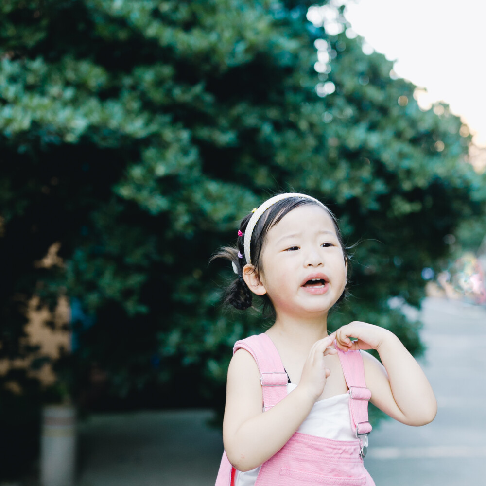 你是我甜而不腻的夏天
摄影：洪小漩
出镜：菲比
生女儿，就是为了能把她打扮得如花花绿绿的糖果一般。阳光下，她与艳阳比明媚，绿荫下，她与梧桐比茂盛。
那日下班到家，天气尚好，我牵着菲比的手在小区楼下散步。说尽好话才请她配合我拍了几张照，期间一颗水果冻起到了八成的作用，剩下的时间都在“拍一张嘛”和“不要不要”之间拉锯。
33个月，不算大，却到了鬼精灵和耍赖皮的年龄段。这时候，她泛起倔来毫无道理可讲，我却只能以“她在守护自己的秩序感”为由，对她的予取予求适当满足。
算了，看在她是我女儿且尚有几分可爱的份上，该抱就抱，想买就买吧。
毕竟，这个阶段太短暂，最主要的是，她要的东西我尚且买得起。