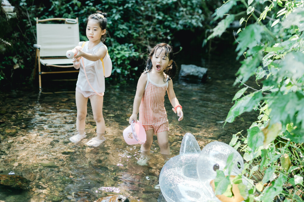 夏天总是要去九溪的
摄影：洪小漩
出镜：菲比和格格等
每年夏天，九溪都是必去之地。
曾经，打车是可以直达九溪烟树的。如今，想要驱车前往，必须提前预约。或是统一乘坐观光车进入。
今日份阿科出差，两个三口之家的出行便缺了一个壮劳力，少了一分从容。
三个大人提着装备吃食，外加菲比三不五时闹着要抱，我们便索性绝了步行进入的念头，半程观光车，半程徒步，总算找了一小片人不算多的水域。
阿科不在，张罗菲比的我显得十分狼狈。不过，小朋友玩得尽兴，别的也就无所谓了。
一只小桶、一把水枪、一个游泳圈、一个西瓜，夏天那味便有了七八分。剩下的便是聒噪的蝉鸣和潺潺的流水。这不，今日都齐了。