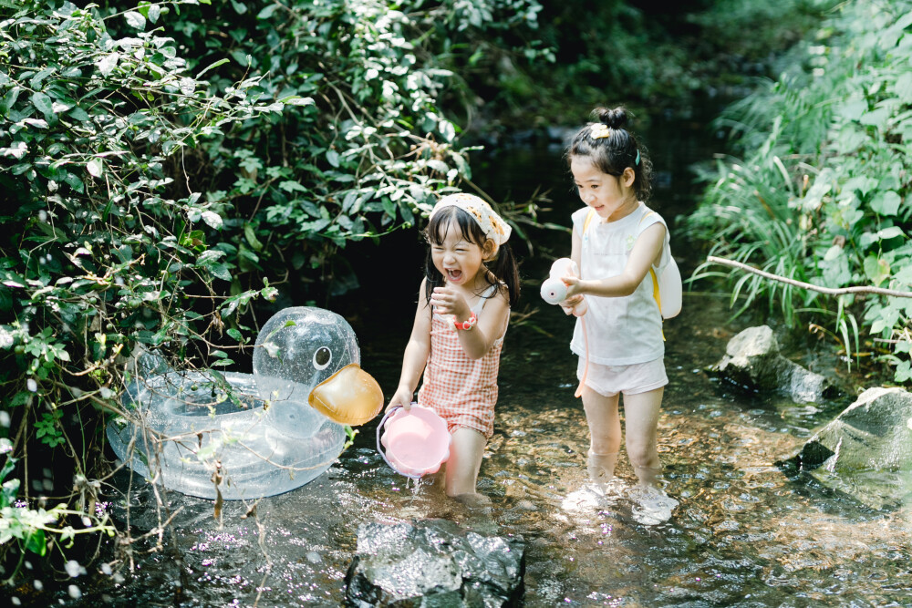 夏天总是要去九溪的
摄影：洪小漩
出镜：菲比和格格等
每年夏天，九溪都是必去之地。
曾经，打车是可以直达九溪烟树的。如今，想要驱车前往，必须提前预约。或是统一乘坐观光车进入。
今日份阿科出差，两个三口之家的出行便缺了一个壮劳力，少了一分从容。
三个大人提着装备吃食，外加菲比三不五时闹着要抱，我们便索性绝了步行进入的念头，半程观光车，半程徒步，总算找了一小片人不算多的水域。
阿科不在，张罗菲比的我显得十分狼狈。不过，小朋友玩得尽兴，别的也就无所谓了。
一只小桶、一把水枪、一个游泳圈、一个西瓜，夏天那味便有了七八分。剩下的便是聒噪的蝉鸣和潺潺的流水。这不，今日都齐了。