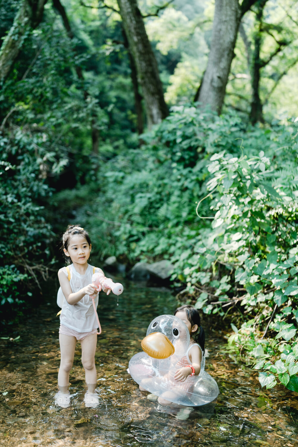 夏天总是要去九溪的
摄影：洪小漩
出镜：菲比和格格等
每年夏天，九溪都是必去之地。
曾经，打车是可以直达九溪烟树的。如今，想要驱车前往，必须提前预约。或是统一乘坐观光车进入。
今日份阿科出差，两个三口之家的出行便缺了一个壮劳力，少了一分从容。
三个大人提着装备吃食，外加菲比三不五时闹着要抱，我们便索性绝了步行进入的念头，半程观光车，半程徒步，总算找了一小片人不算多的水域。
阿科不在，张罗菲比的我显得十分狼狈。不过，小朋友玩得尽兴，别的也就无所谓了。
一只小桶、一把水枪、一个游泳圈、一个西瓜，夏天那味便有了七八分。剩下的便是聒噪的蝉鸣和潺潺的流水。这不，今日都齐了。